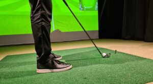 A closeup shot of a male golfer playing golf indoors on a golf simulator, driving the ball.